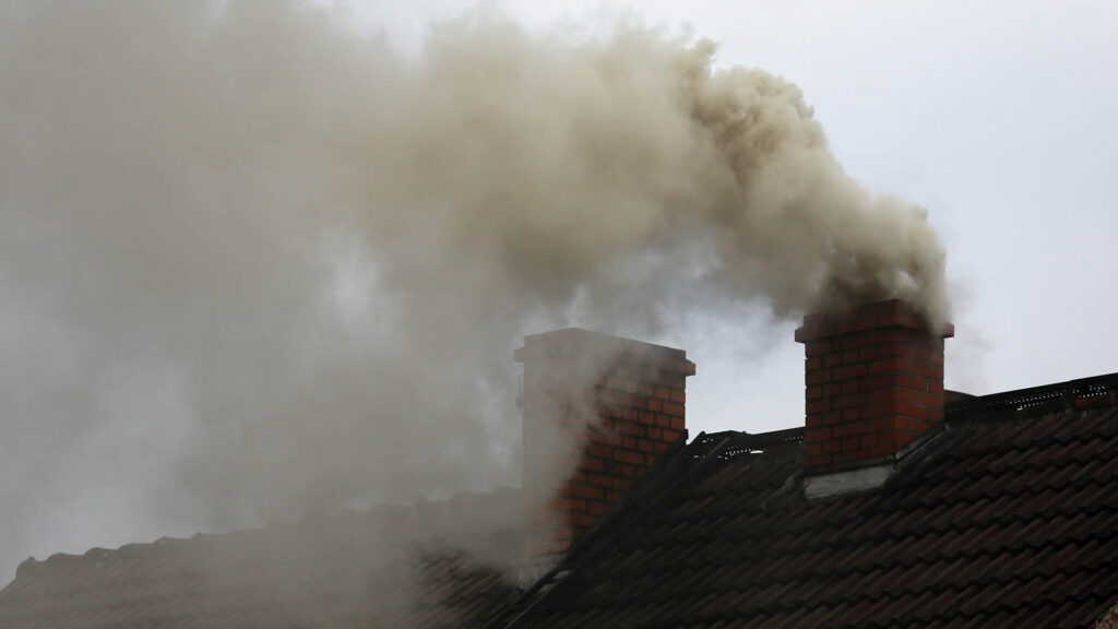 Two chimneys made of red bricks are seen producing dark gray smoke.