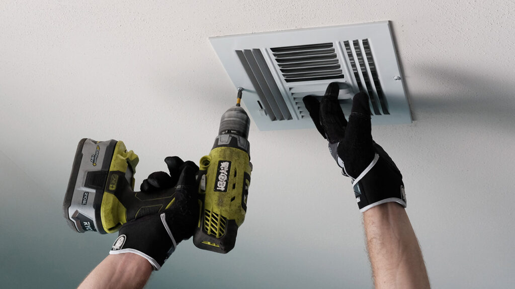 Person using a screwdriver on the grate of an air duct.