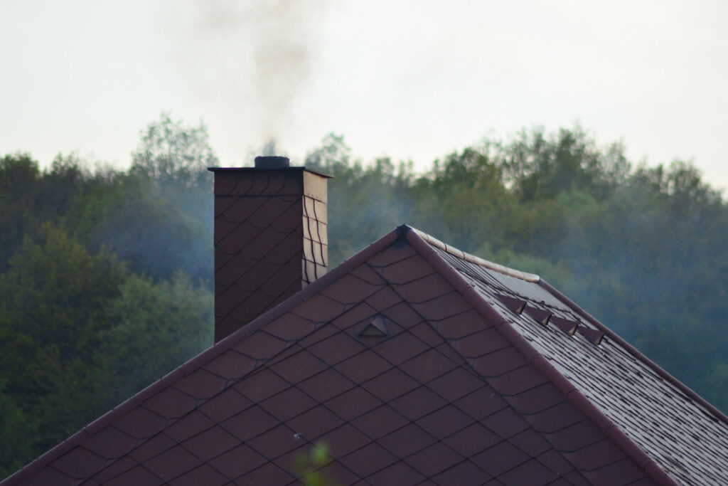 View of a chimney with smoke coming out of the top next to a skyline with trees.