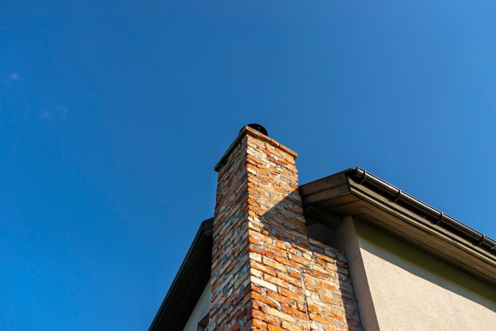 A low-angle view of a brick chimney against a cloudless blue sky.
